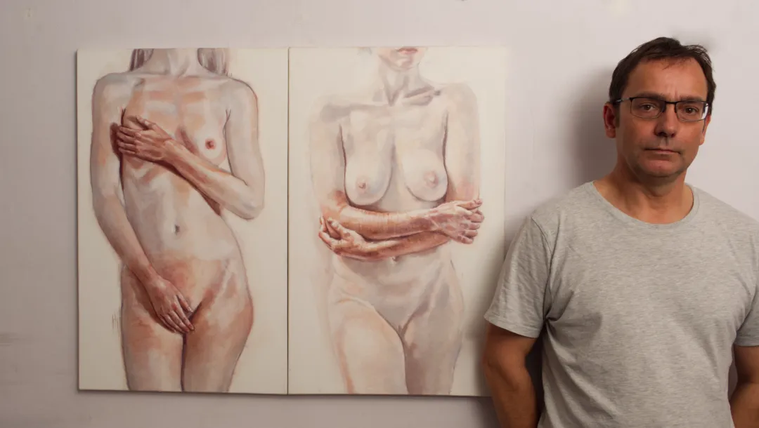 artist standing next to two paintings of headless nude portraits